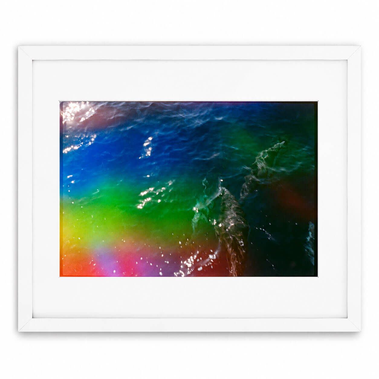 A framed art print featuring an aerial photograph of dolphins swimming in vibrant, rainbow-colored water, presented in a white frame with a white mat against a clean white background.